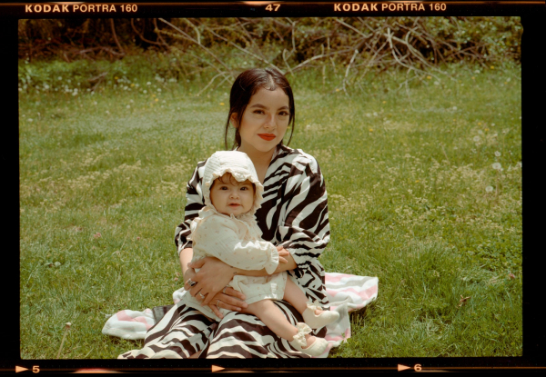 portrait of a woman and her baby sitting in a grass field. the woman wears a zebra stripe dress and red lipstick the...