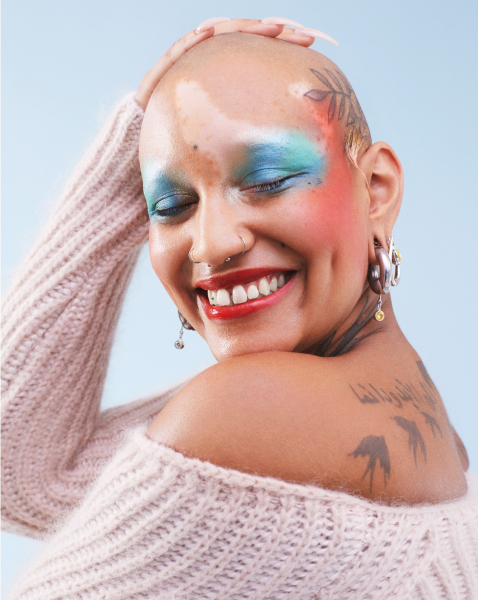 portrait of a bald person with tattoos on their head and back wearing watercolor coral and blue makeup and an...